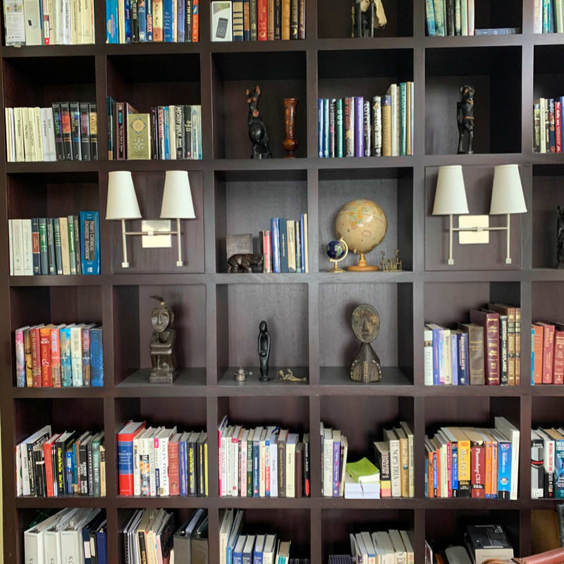 A dark brown grid bookshelf is filled with various books, decorative figurines, a globe, and two small lamps.