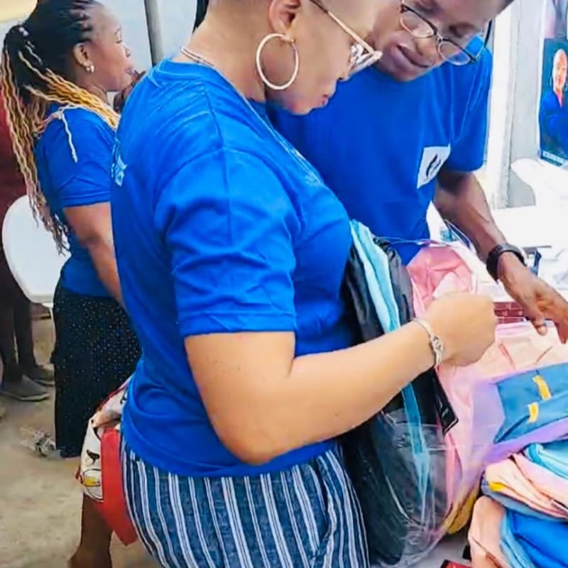 Two people in blue shirts organize colorful clothing in the foreground against a plain, light-colored wall in the background.