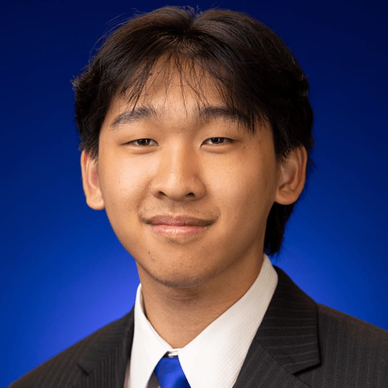 A young man in a suit and tie poses against a solid blue background.