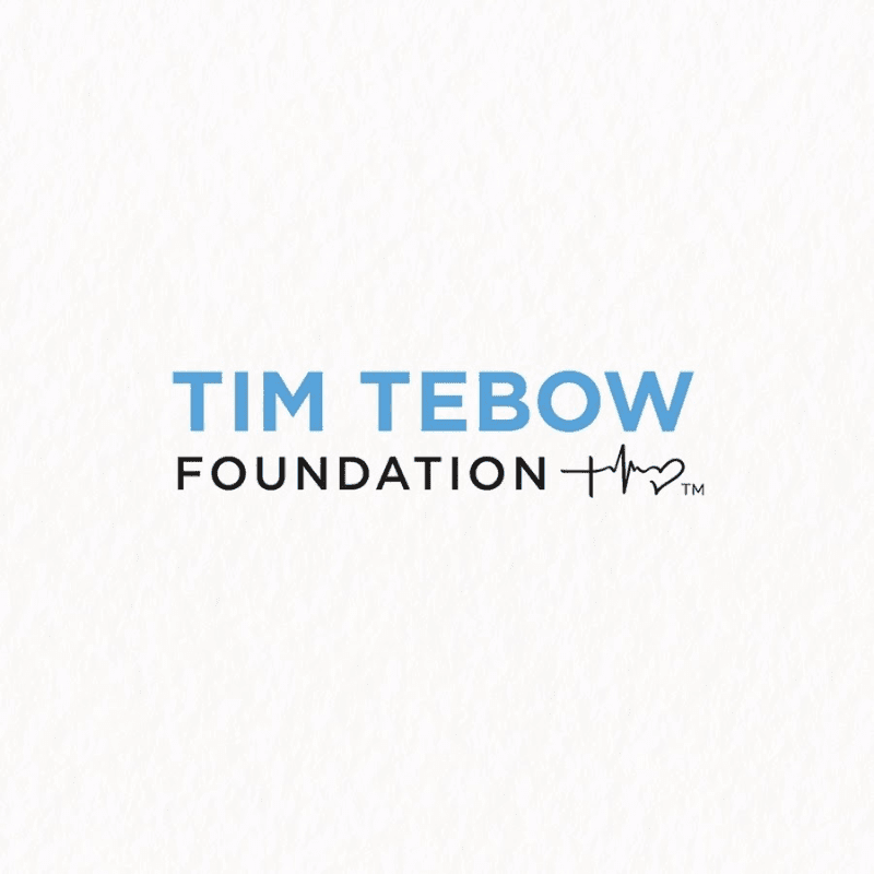 The Tim Tebow Foundation logo, featuring blue and black text with a heart-shaped heartbeat line, is centered on a textured white background.