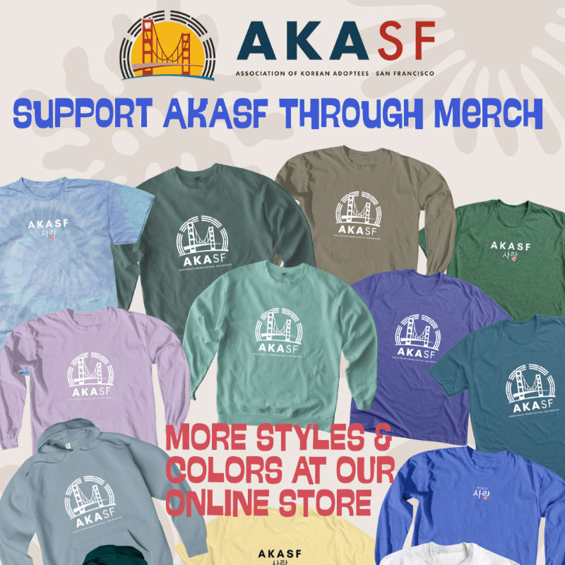 Various colorful AKASF branded shirts and sweatshirts are displayed in the foreground against a light-colored background featuring the organization's logo and a promotional message.
