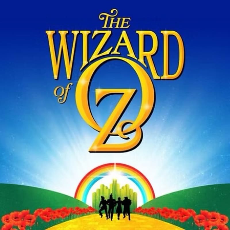 Silhouetted figures walk down a yellow brick road lined with red poppies towards a rainbow and the Emerald City, all under the title "The Wizard of Oz" against a bright blue sky.