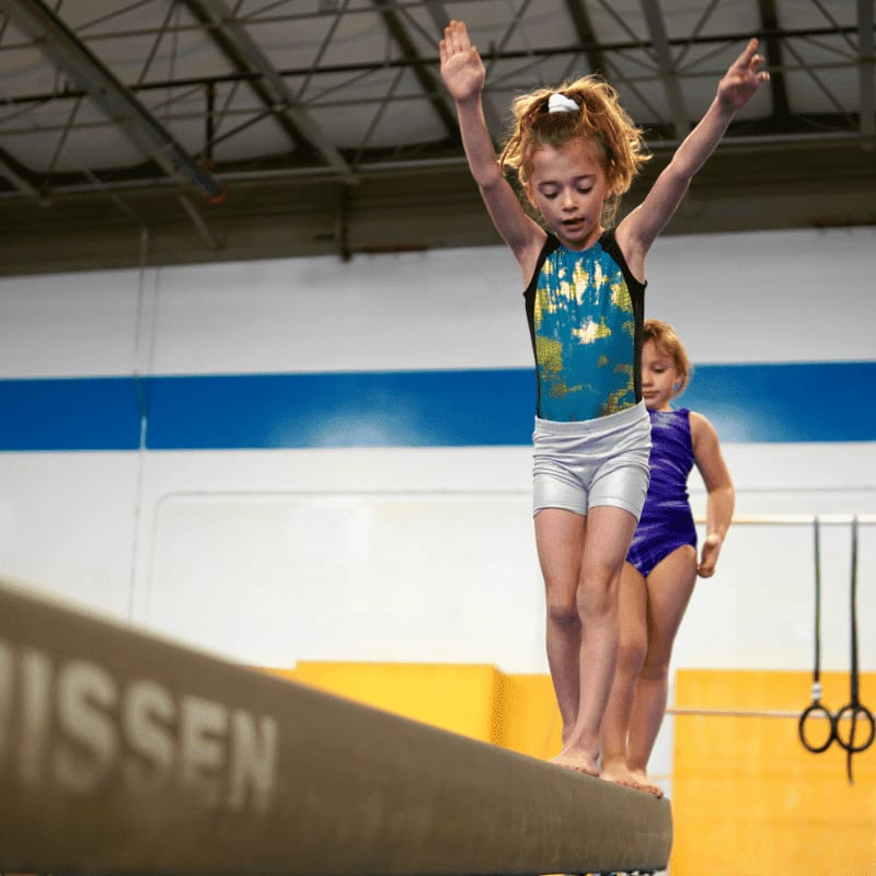 a person jumping on a trampoline with a child in the background