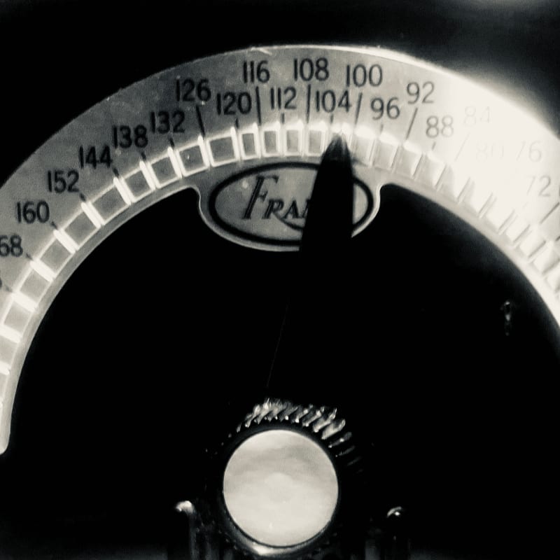 A close-up of a radio dial with a pointer and numbers in the foreground against a dark, shadowed background.
