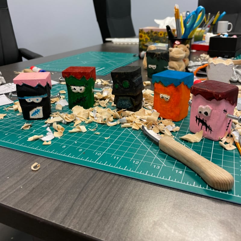 A wooden bear carving sits on the left, while a fiery spirit carving and a knife rest on wood shavings on the right, with the word "CARVE" vertically centered.