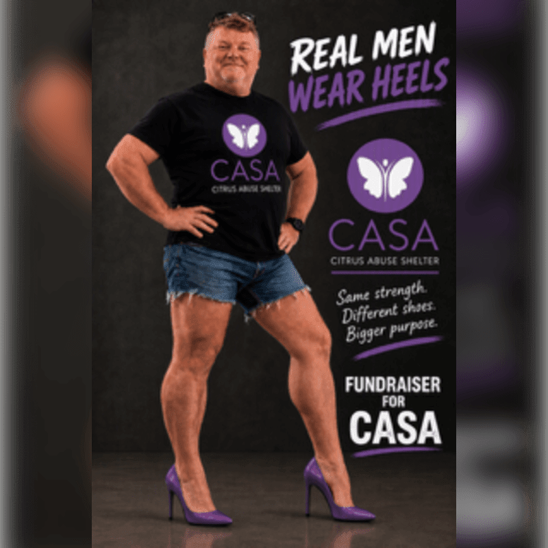 A man wearing a CASA t-shirt, denim shorts, and purple high heels stands in the foreground against a dark grey background with promotional text and logos.