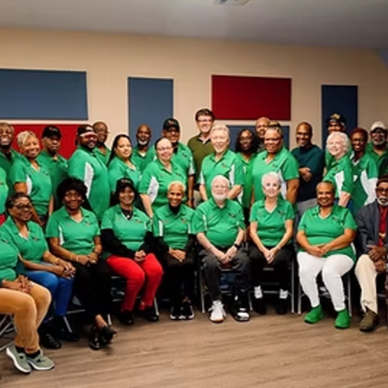 A group of people wearing green shirts pose for a photo in a room with blue and red rectangular wall panels.