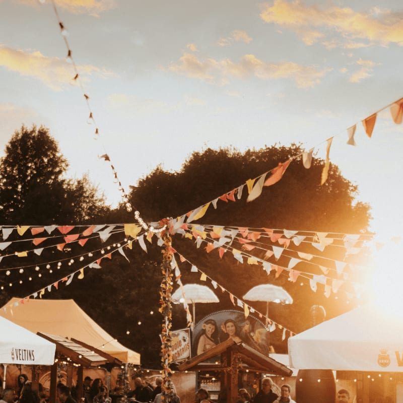 Colorful bunting flags strung above festival stalls under a warm golden sky