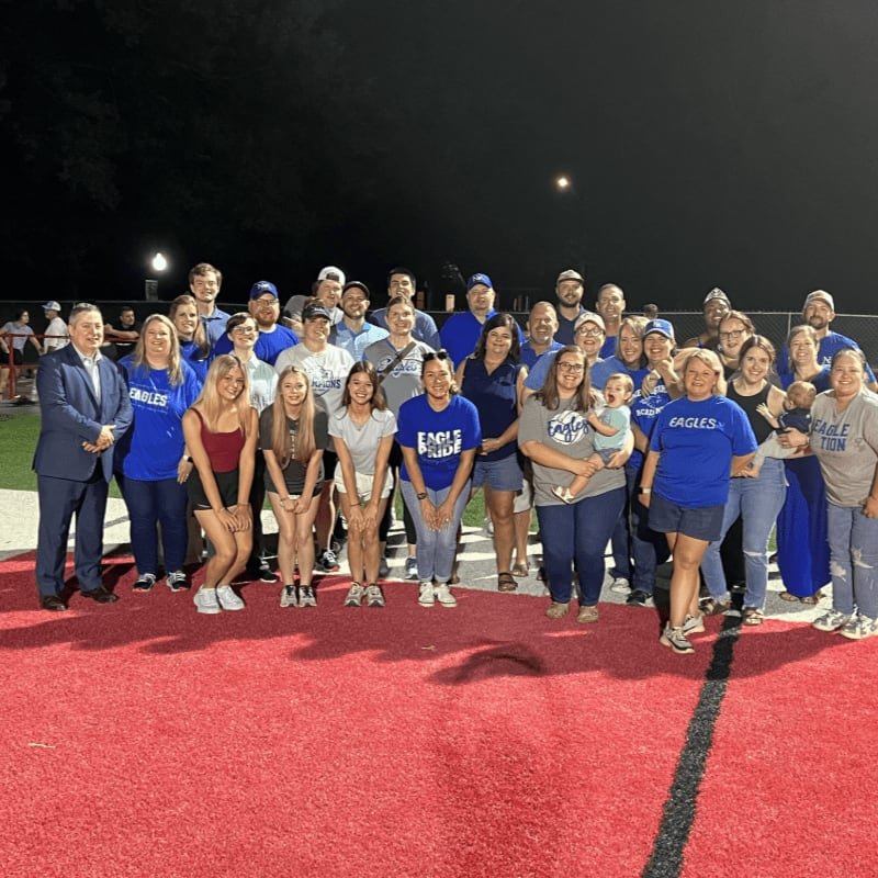 A large group of people pose for a photo on a red athletic track against a dark night sky.