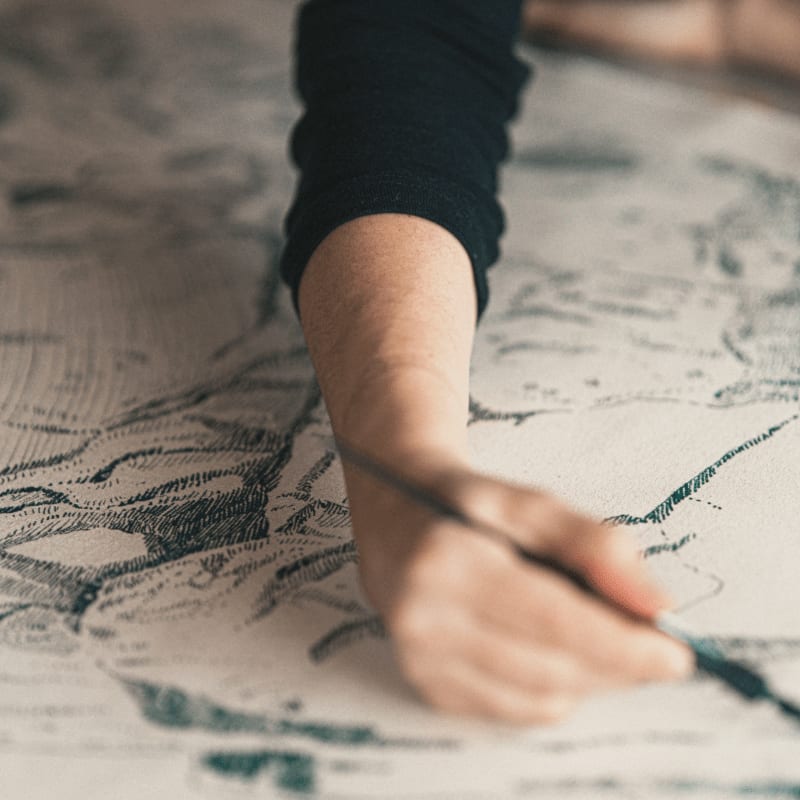 A person's arm and hand hold a pencil over a detailed sketch on a white surface.