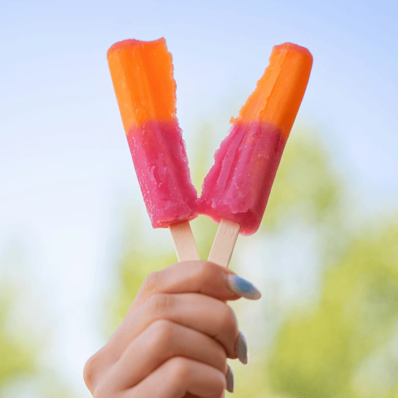 Hand holding two colorful, partially eaten popsicles