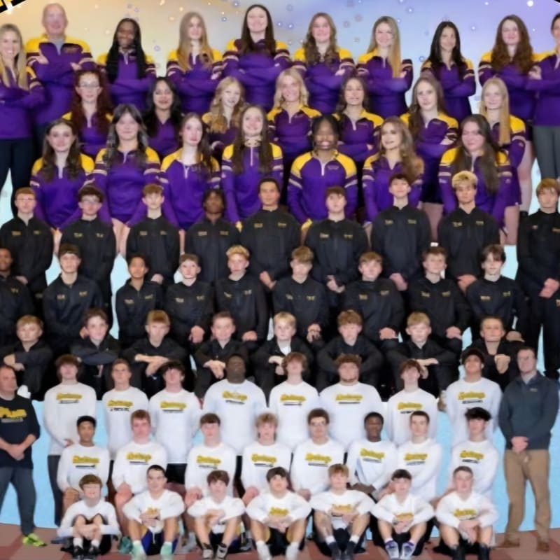 A large group of athletes in purple and black uniforms and white t-shirts pose for a team photo against a light-colored, sparkling background.