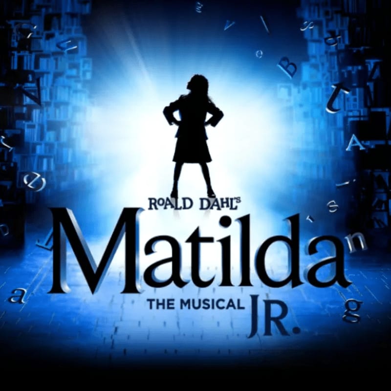 The title "Matilda The Musical JR." sits in the foreground beneath the silhouette of a young girl standing against a glowing blue background of floating letters and bookshelves.