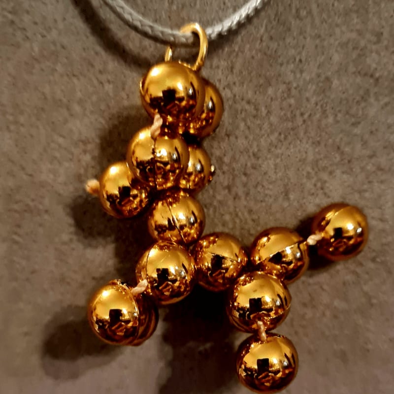 A gold-colored beaded pendant hangs from a grey cord against a textured grey background.