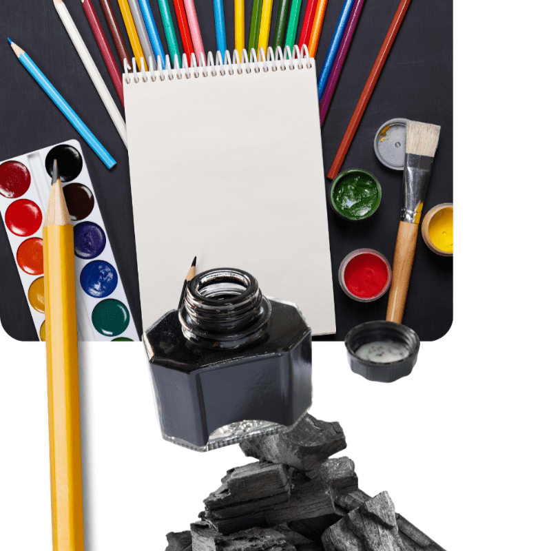 An ink bottle, charcoal, and a yellow pencil sit in the foreground against a background of a blank notebook, colored pencils, and paint supplies on a black surface.