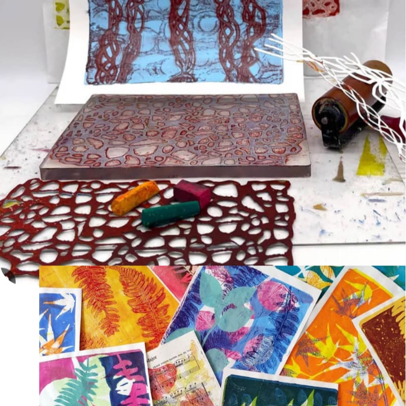 Art supplies and a printing block sit on a white table in the foreground, with a finished print and a collection of colorful botanical artworks in the background.