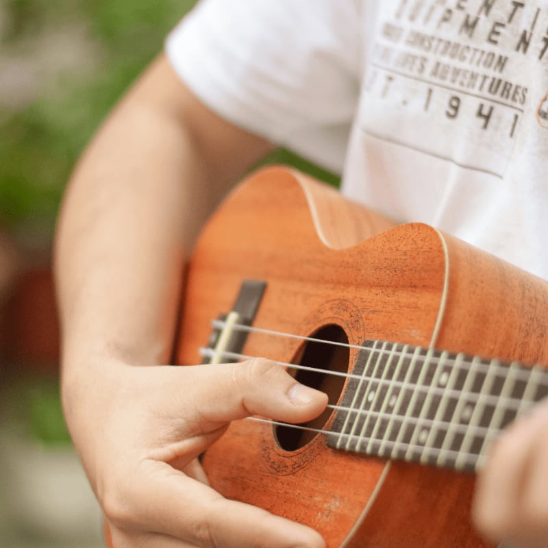 person in white t-shirt playing brown acoustic guitar