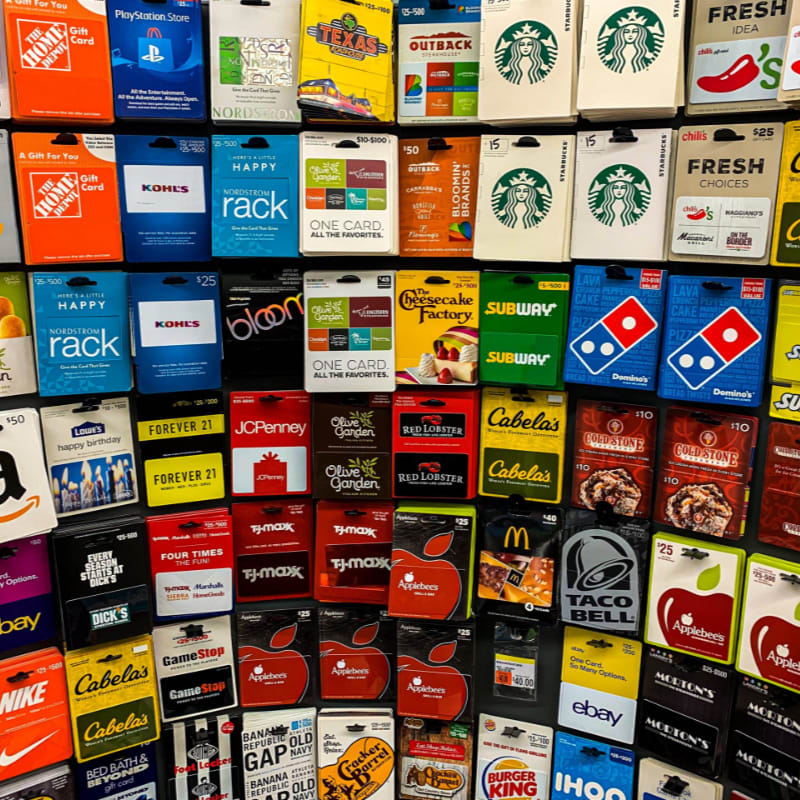 A dense grid of various colorful gift cards fills the foreground, set against a dark, structured display rack in the background.
