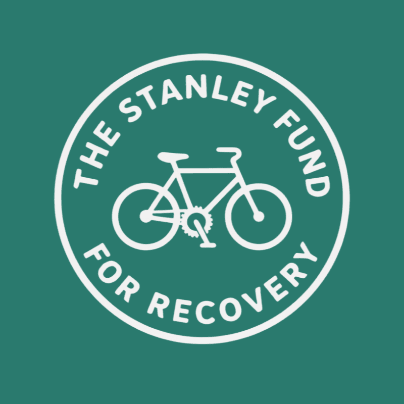 A white circular logo featuring a bicycle and the text "THE STANLEY FUND FOR RECOVERY" is centered on a solid green background.