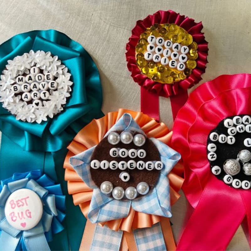 Several colorful handmade award ribbons with beaded text sit on a neutral, textured background.