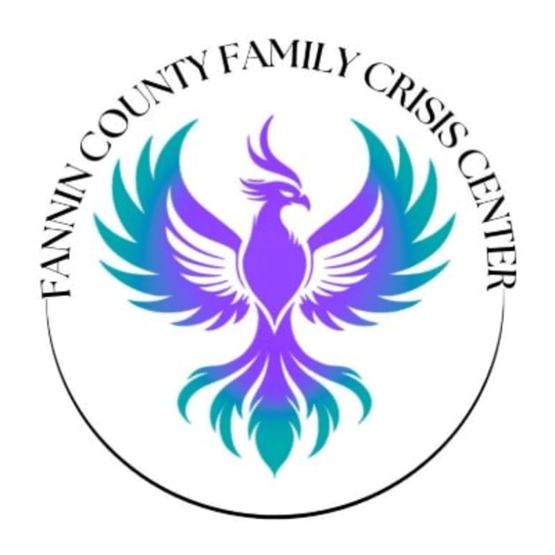 A purple and teal phoenix with outstretched wings is centered within a black circle, surrounded by the text "FANNIN COUNTY FAMILY CRISIS CENTER" in white.