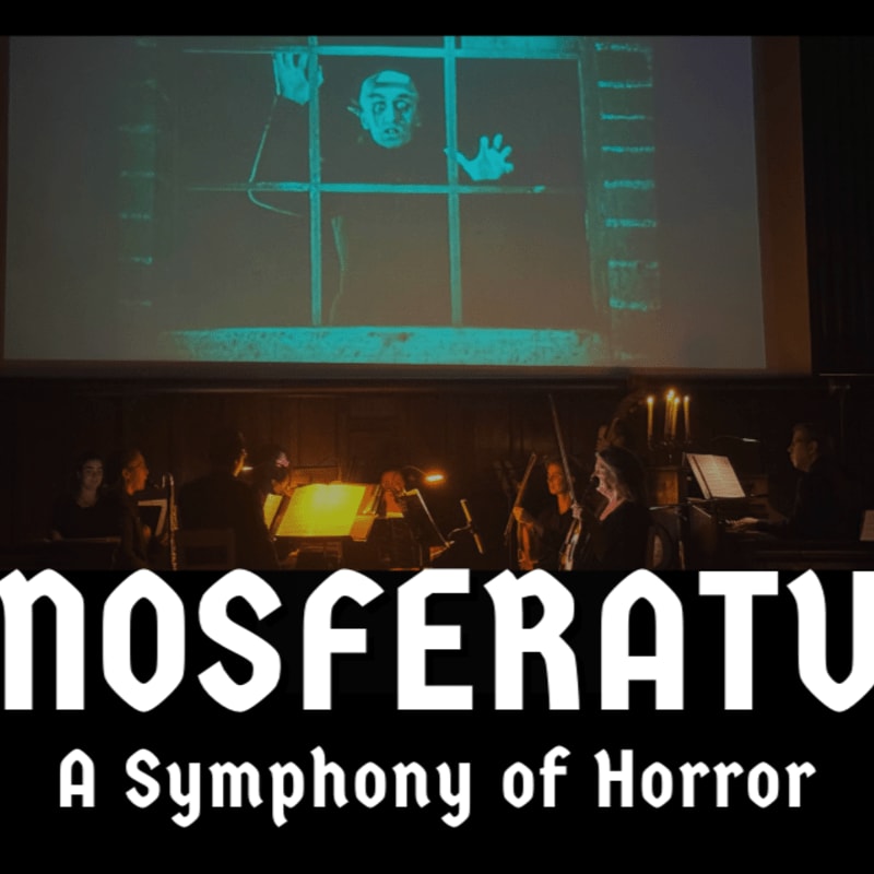 An orchestra performs in a dimly lit foreground beneath a large projection of a pale figure behind bars.