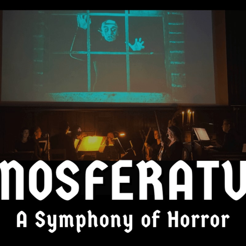 An orchestra performs in a dimly lit foreground beneath a large projection of a pale figure behind bars.