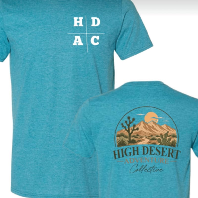 A turquoise t-shirt with a white "HDAC" logo on the chest is positioned in the foreground, while the back of the same shirt featuring a desert landscape graphic is shown behind it.