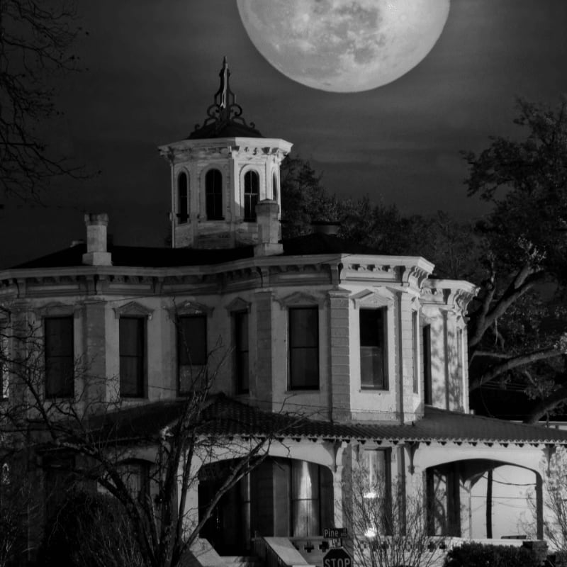 A spooky, old Victorian mansion stands in the foreground under a massive, glowing full moon in the dark night sky.