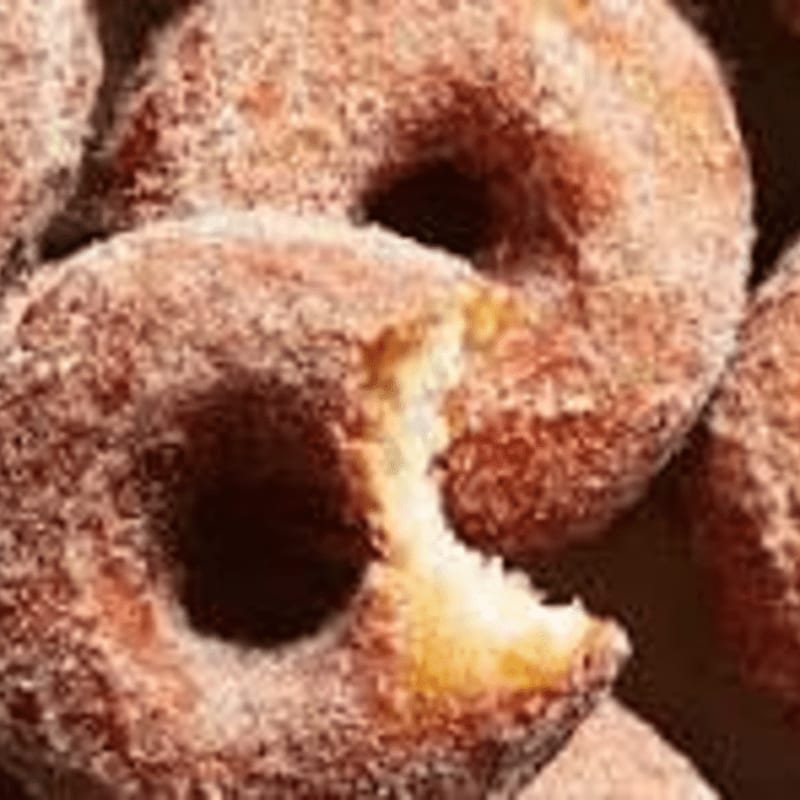 A bitten cinnamon-sugar donut sits in the foreground, surrounded by several whole donuts in the background.