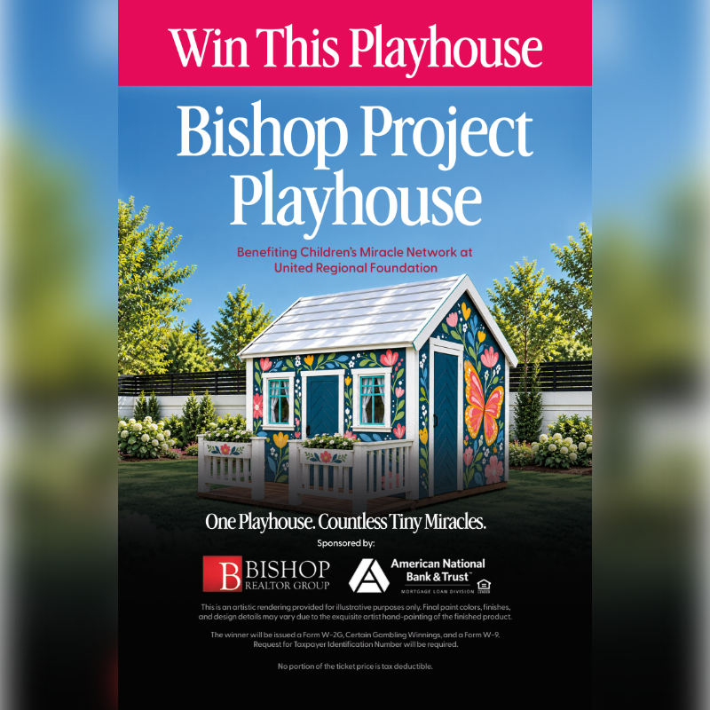 A colorful, hand-painted playhouse sits in a grassy yard with white flowers and green trees under a blue sky.
