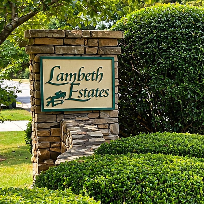 A stone pillar with a "Lambeth Estates" sign stands in the foreground, surrounded by lush green bushes and trees in the background.