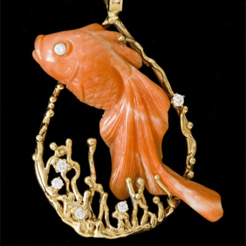 An orange coral fish pendant with gold accents and diamonds is set against a solid black background.