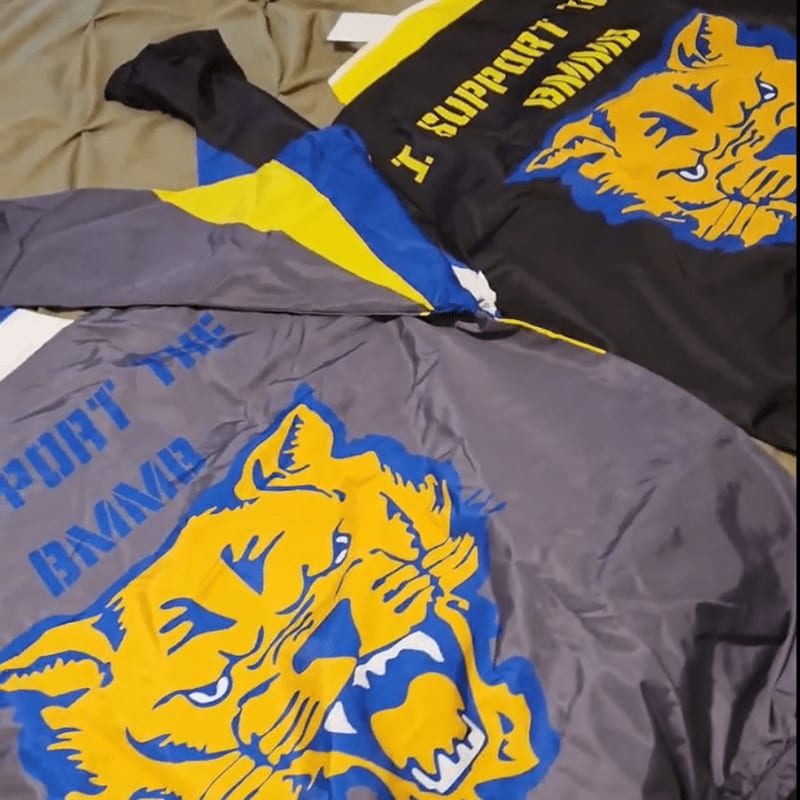 Two athletic shirts featuring a yellow and blue tiger logo lie folded on a tan fabric surface.