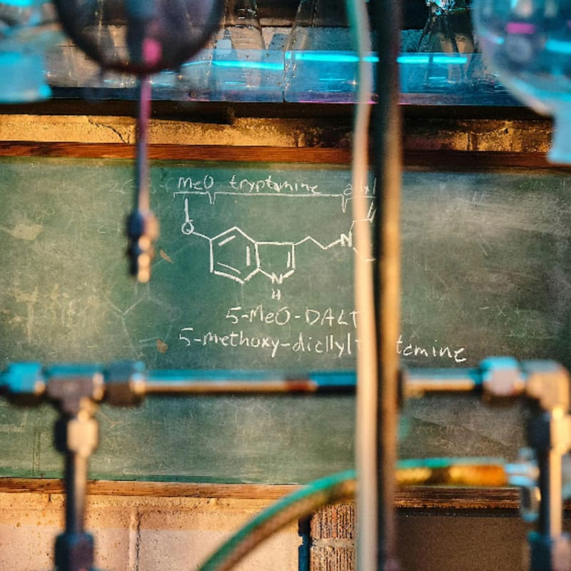 Metal pipes and tubing frame a green chalkboard featuring a hand-drawn chemical structure and text.