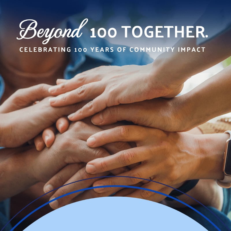 Multiple hands are stacked together in the foreground against a blurred background of people, with celebratory text overlaying the top.