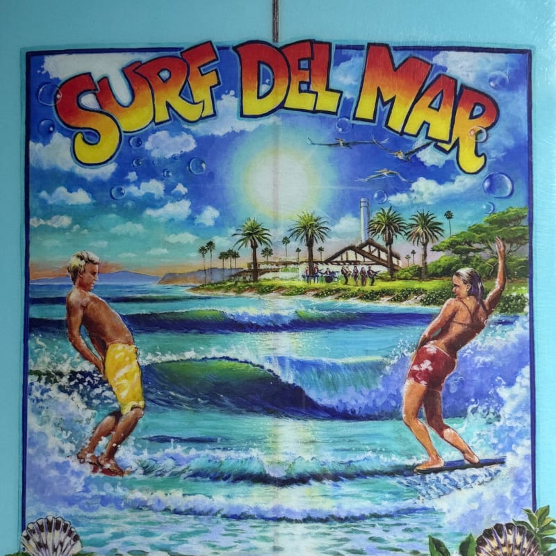 Two surfers ride waves in the foreground of a tropical beach scene featuring palm trees, a pier, and a bright sun under the words "SURF DEL MAR."