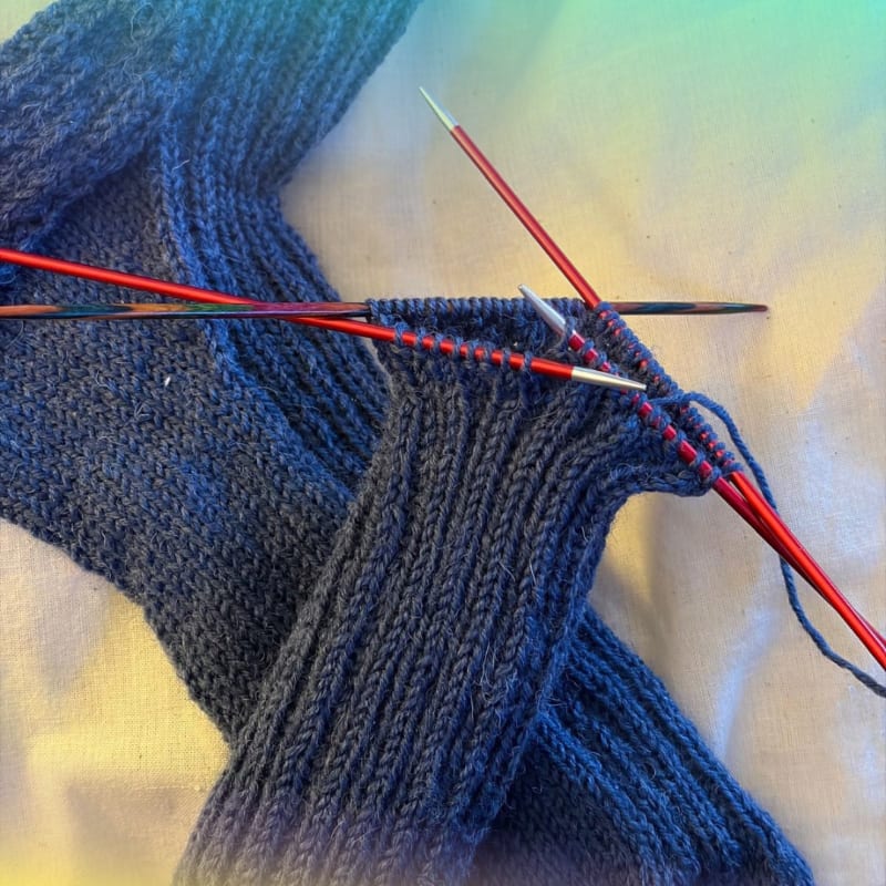 Blue knitted fabric on red and silver needles rests against a light-colored fabric background.