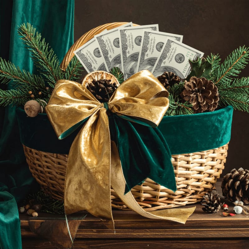 A wicker basket filled with US dollar bills and pine branches, adorned with a large gold and green bow, sits against a dark brown background.