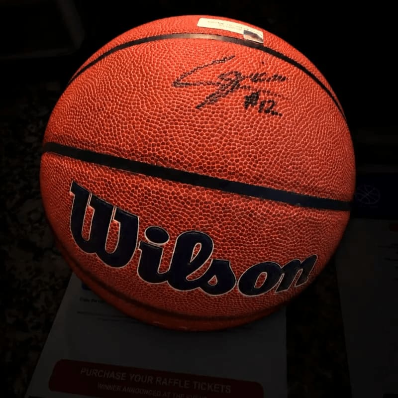 An orange Wilson basketball with a signature sits in the foreground against a dark, blurred background.