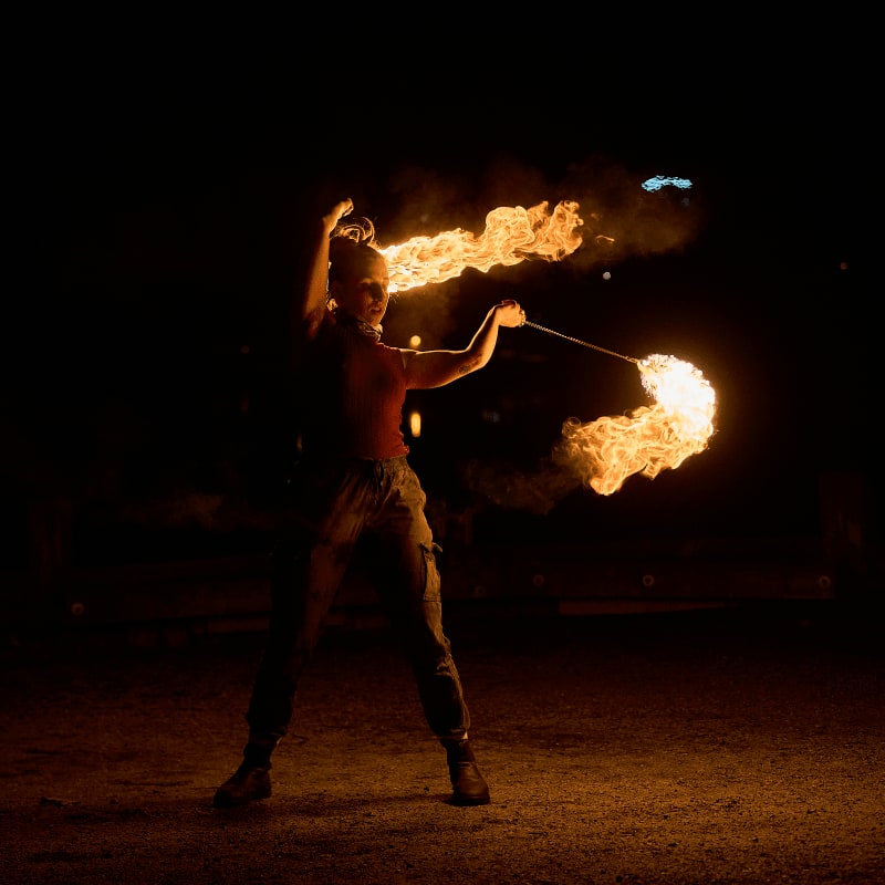 A fire performer swirls flaming torches against a dark, nighttime background.