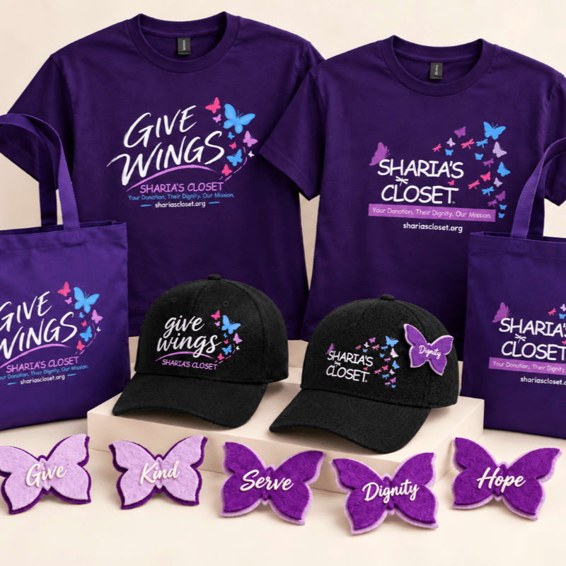 Purple t-shirts, tote bags, and black baseball caps with "Give Wings" and "Sharia's Closet" branding are arranged in the foreground and background, with small purple butterfly patches lined up at the bottom.