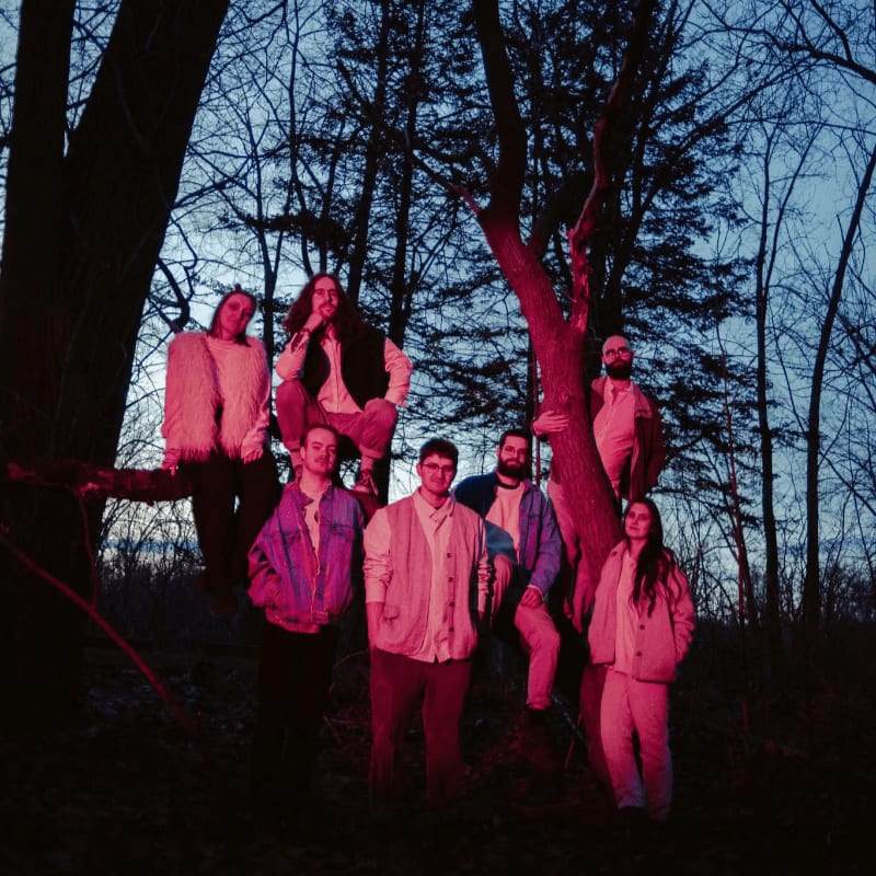 A group of people pose together in a wooded area under a dark blue twilight sky, illuminated by a red light.