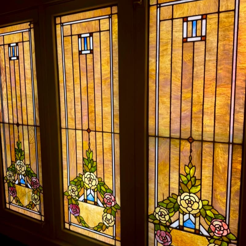 Three ornate stained-glass panels featuring floral designs in the foreground are set within a dark wooden frame in the background.
