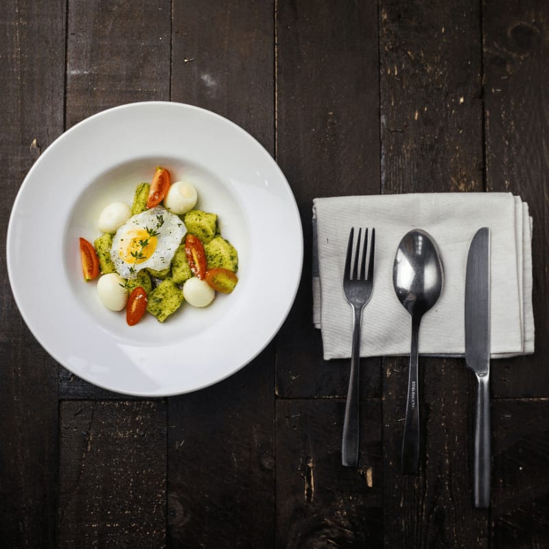 sunny side up egg, boiled quail eggs, sliced red tomatoes, and sliced green bell pepper inside round white ceramic plate in a fine dining set
