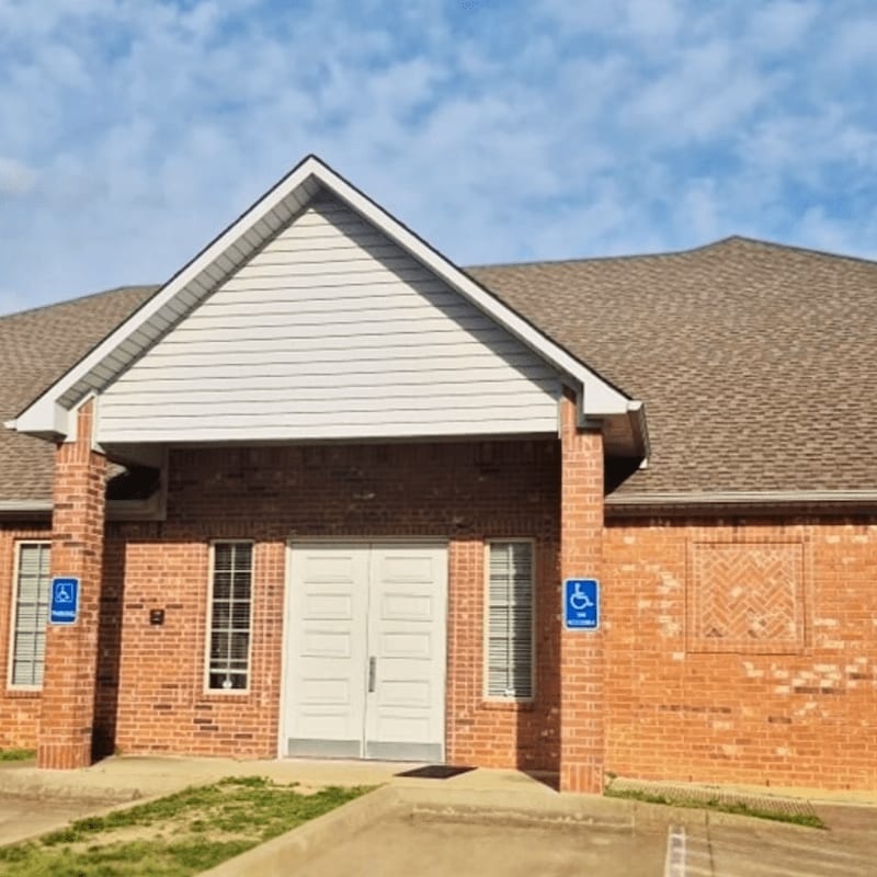 A brick building with white double doors and handicap signs stands under a blue sky with light clouds.
