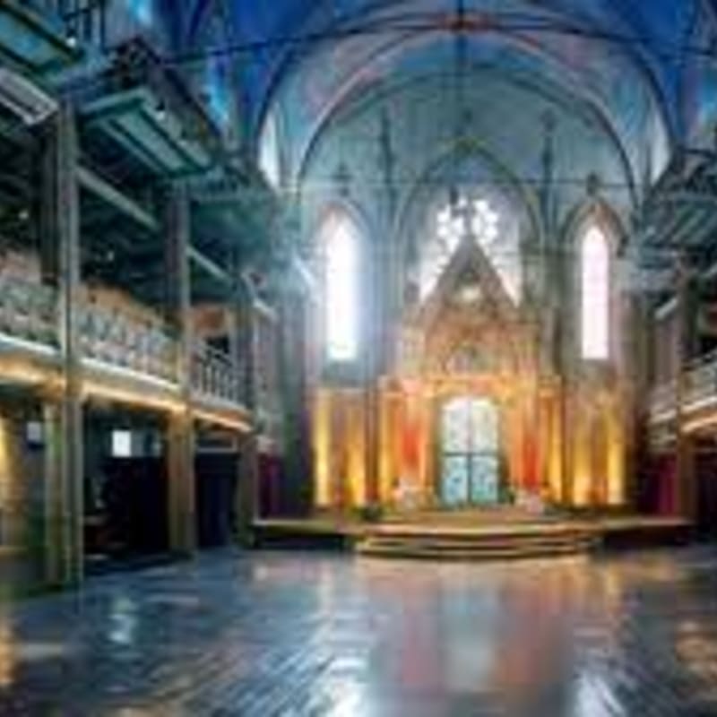 A polished wooden floor leads toward a glowing altar and gothic windows under a vaulted blue ceiling.