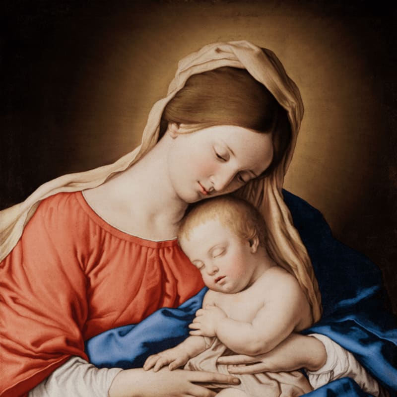 A woman in a red dress and beige veil tenderly holds a sleeping infant against a dark, muted background.