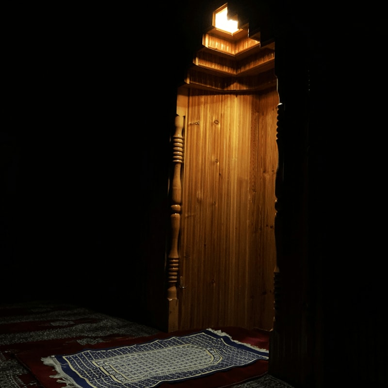 A prayer rug on a red carpet before a wooden mihrab niche