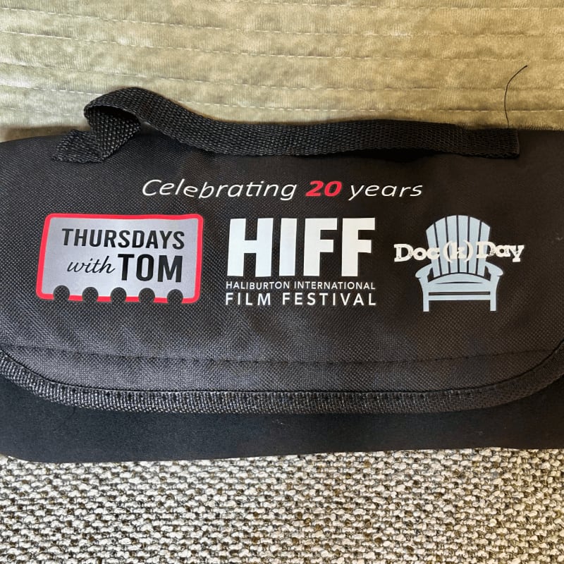 A black fabric bag featuring the Haliburton International Film Festival logo and other text rests on a textured, neutral-toned surface.